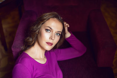 Young tall woman is sitting on a chair in a hotel near the window in tight purple yoga clothes