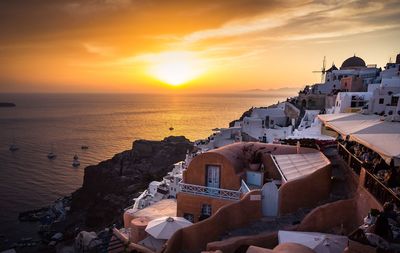 Buildings by sea against sky during sunset