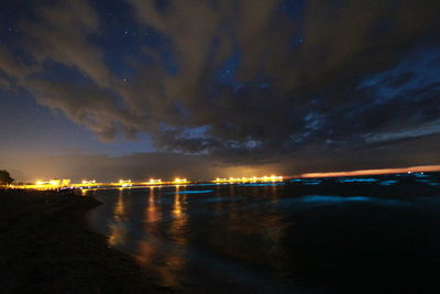 Illuminated city by sea against sky at night