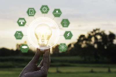 Close-up of hand holding light bulb against sky