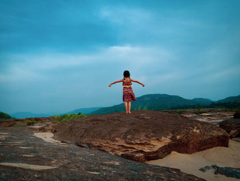 Rear view of man standing on rock against sky