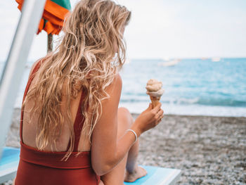 Woman with ice cream sitting on lounge chair at beach