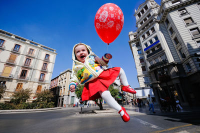 Girl with balloon in mid-air against building against blue sky