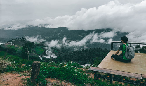 Rear view of man sitting against mountain and sky