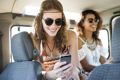 Woman using mobile phone while sitting with female friend in off-road vehicle