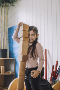 Smiling girl stacking wooden toy blocks in kindergarten