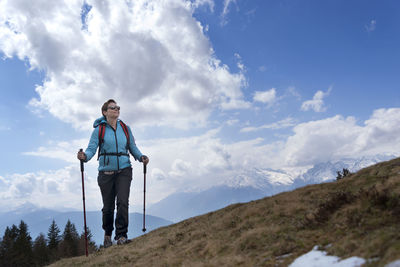 Female hiker walking on mountain against cloudy sky