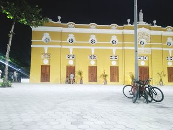 Bicycle parked on illuminated street by buildings at night