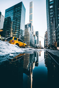 Car on snowy street by reflection against buildings