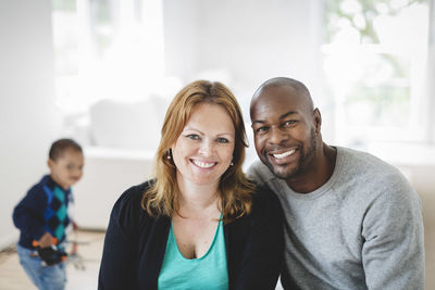 Portrait of multi-ethnic couple sitting at home with son in background