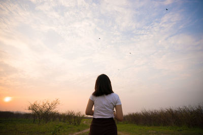 Rear view of woman standing on field against sky