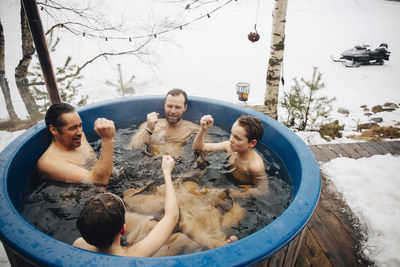 Mature men with boys gesturing fists while taking bath in hot tub