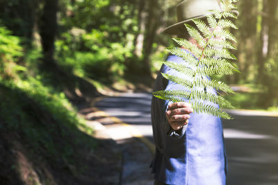 Man in the forest covers his face with a fern leaf.