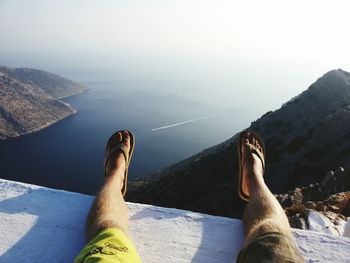 Low section of man sitting on retaining wall against sea