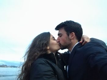 Side view of young couple kissing against clear sky