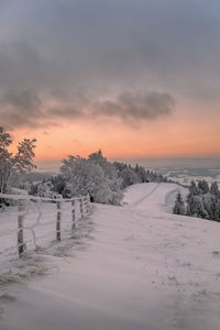 Snow covered field against sky during sunset