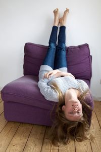 Portrait of teenager lying on purple lounge chair against white wall at home