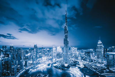 Illuminated buildings in city against cloudy sky