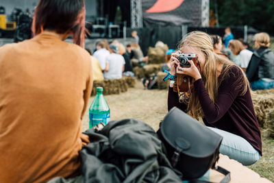 Woman photographing friend while sitting at park