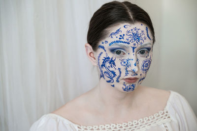 Portrait of woman with painted face against curtain at home