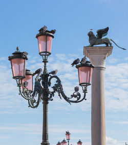 Low angle view of birds perching on street light against sky