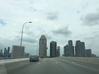Road passing through city against cloudy sky