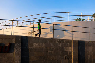 Full length of sweeper with broom walking by railing