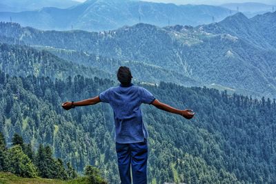 Rear view of man with arms outstretched standing on mountain