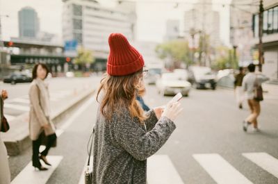 Side view of woman using phone while crossing road in city