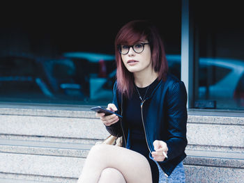 Portrait of woman using mobile phone and flicking cigarette while sitting on bench