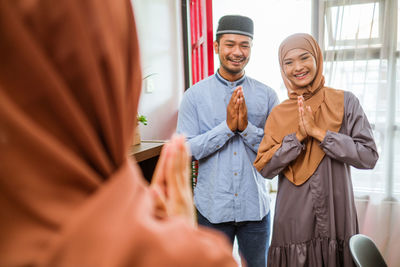 Rear view of couple greeting guest at home