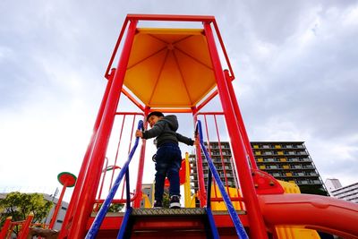 Low angle view of boy standing on outdoor play equipment against sky at playground