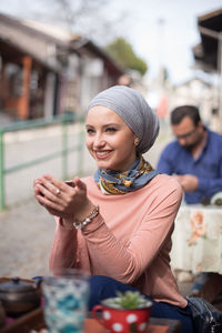 Smiling young woman wearing headscarf while sitting at table