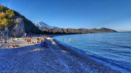 People on beach against clear blue sky