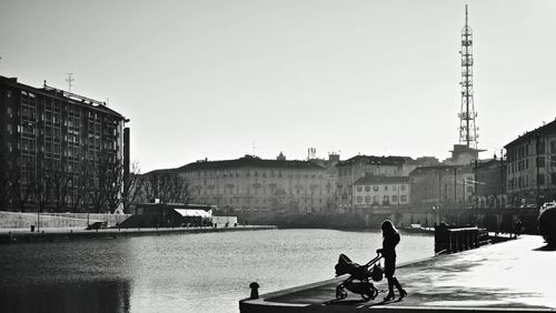 Woman with baby carriage by river in city