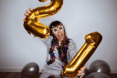 Portrait of cheerful woman holding balloons while sitting against wall at home