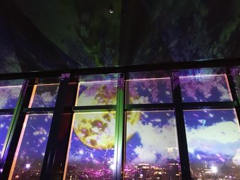 Low angle view of glass window against illuminated building