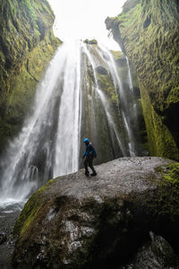 Woman standing on rock against waterfall