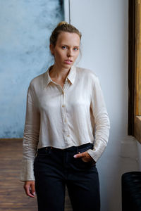 Portrait of young woman standing against wall at home