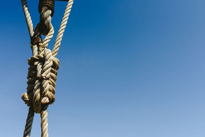 Low angle view of rope tied up against blue sky