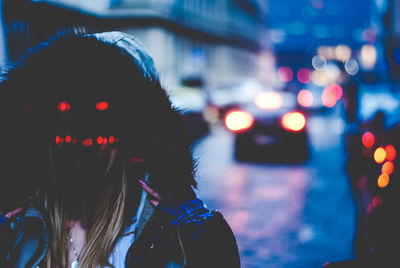 Woman wearing spooky illuminated mask on street at dusk