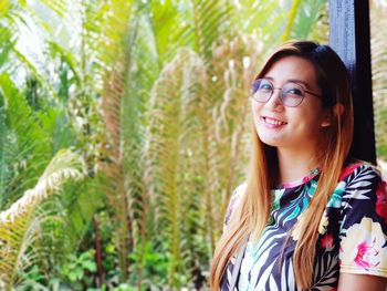 Portrait of smiling young woman standing against plants