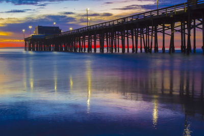 Illuminated pier over sea against sky during sunset