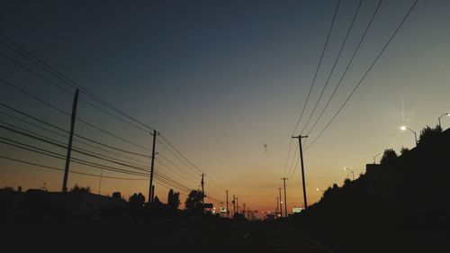 Silhouette electricity pylons against sky at sunset