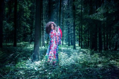 Portrait of woman standing amidst plants against trees in forest