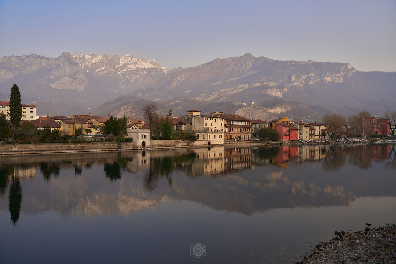 water, reflection, mountain, architecture, morning, building, sky, building exterior, built structure, lake, nature, mountain range, landscape, city, scenics - nature, travel destinations, house, environment, beauty in nature, dusk, travel, no people, religion, land, outdoors, tranquility, residential district, tourism, clear sky, history, tree, town, twilight, the past, blue