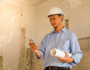 Young man using mobile phone while standing at construction site