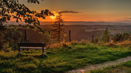 Bench on field against sky during sunset