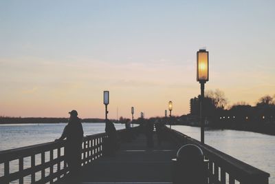 Man by river in city against sky during sunset