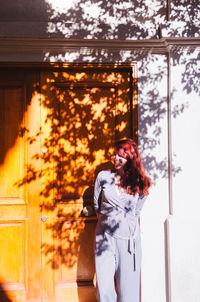 Smiling woman looking away while standing against wall outdoors